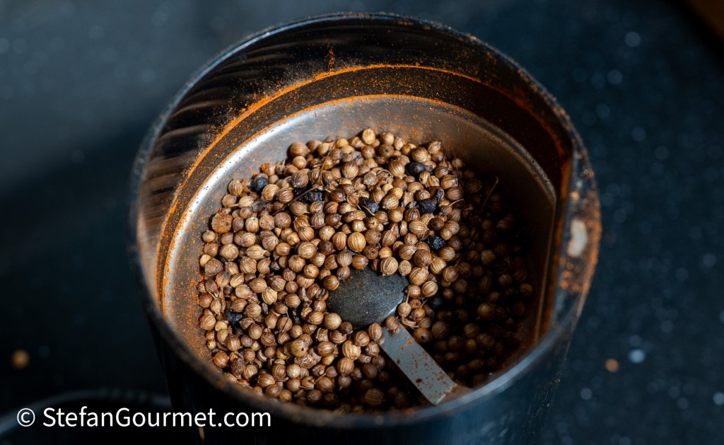 Close-up of coriander seeds and ground spices in a spice grinder.