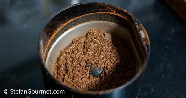 Close-up of ground spices in a small grinder, showcasing a fine texture and dark color.