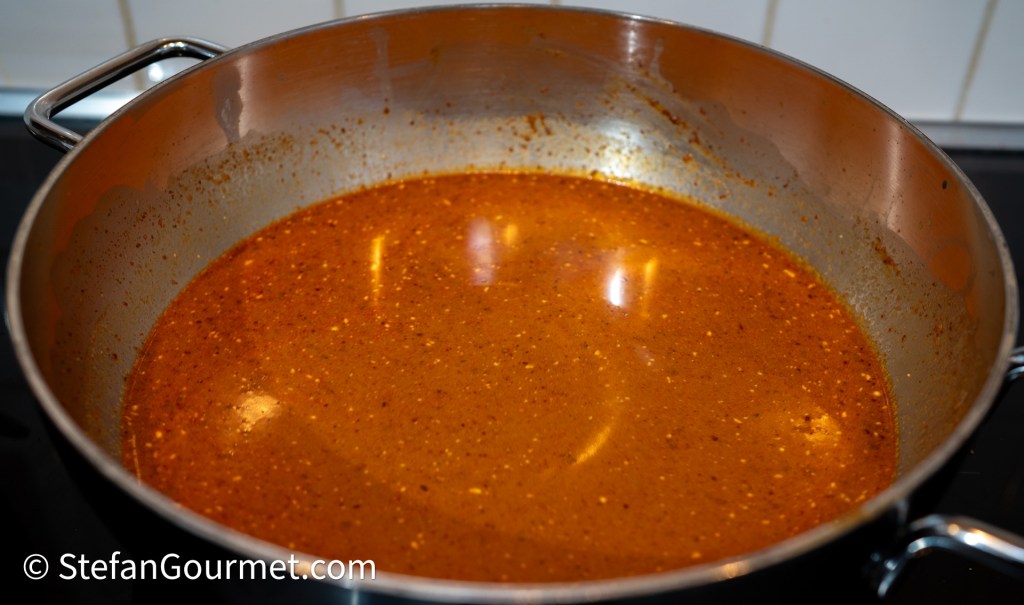 A simmering pot of rich, flavorful curry broth, showing a deep orange color with spices and texture.