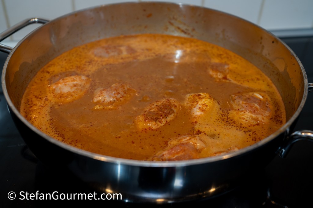 A pot of Khao Soi, a rich curry noodle soup, simmering with chicken pieces in a flavorful broth.