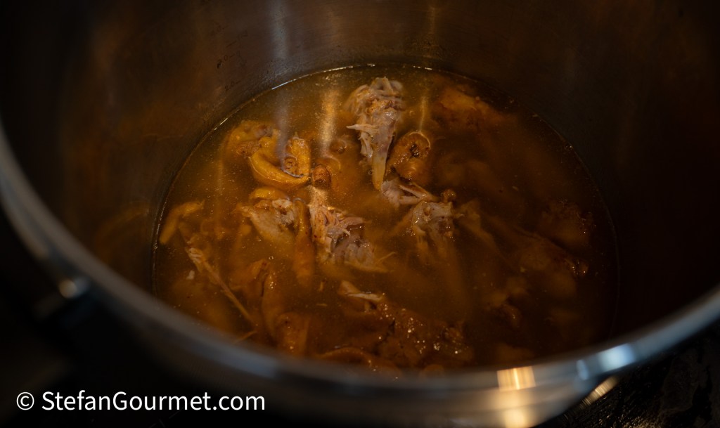 A pot of simmering chicken bones and broth for making Khao Soi, featuring tender chicken pieces submerged in flavorful liquid.