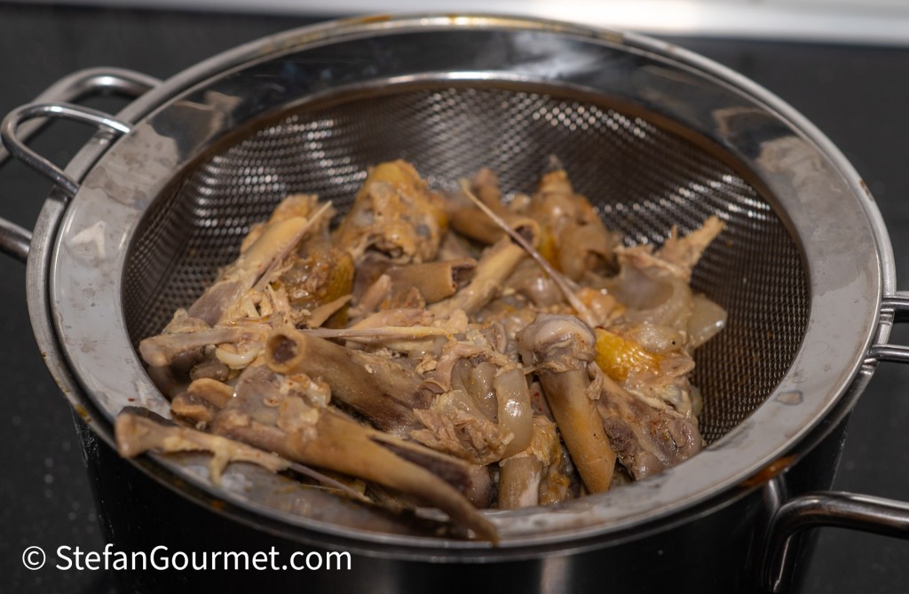 A strainer containing cooked chicken bones and remnants, used for making stock for Khao Soi.