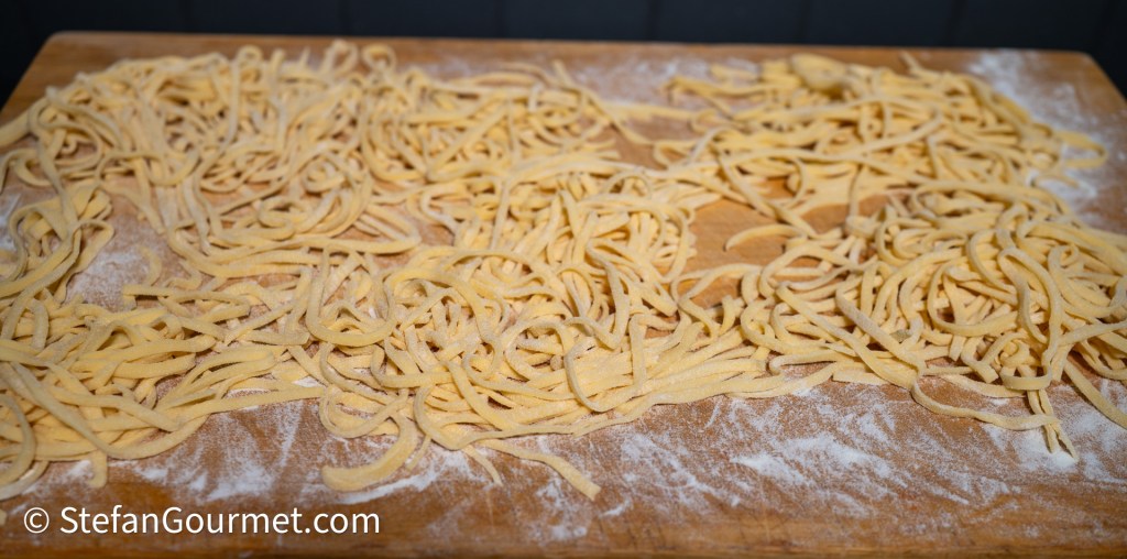 Freshly made egg noodles spread out on a dusted wooden surface.