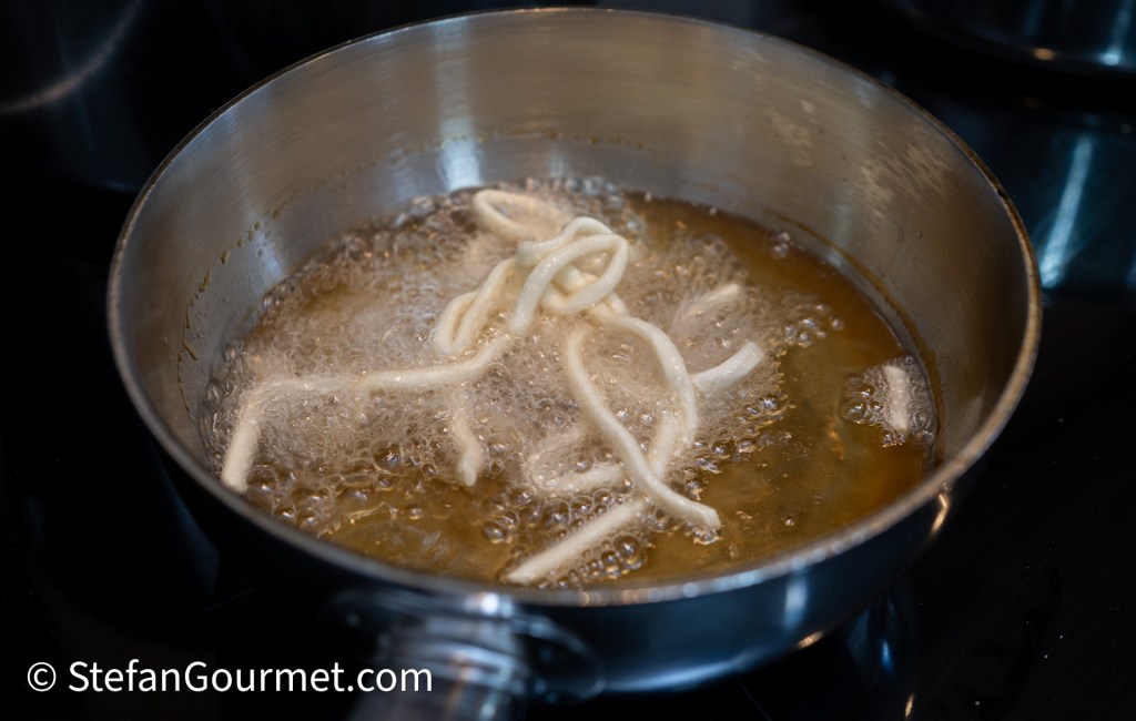 Fresh egg noodles frying in hot oil, bubbling and turning golden brown.