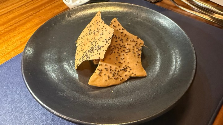 A plate featuring two pieces of crispy, golden-brown wafers sprinkled with small black seeds, artistically arranged.