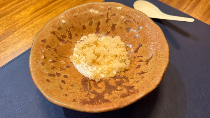 A small bowl with a granita made from coconut sugar, placed on a blue surface, accompanied by a spoon.
