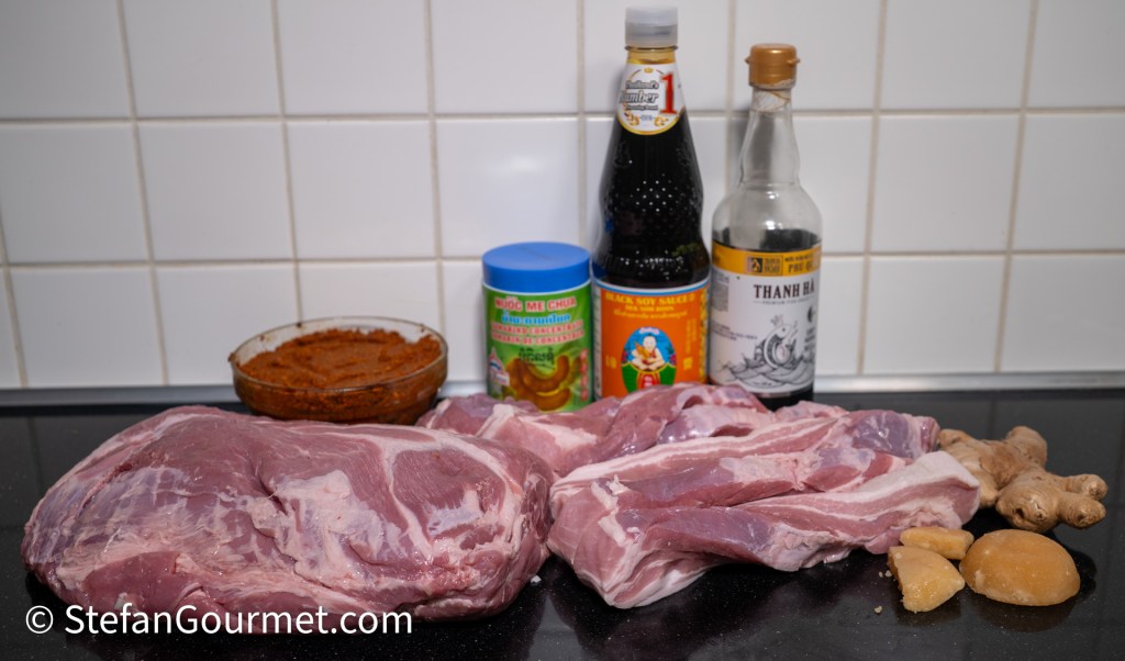 A selection of ingredients for Gaeng Hung Lay curry, including pieces of pork belly, ginger, soy sauce, tamarind paste, and a bowl of curry paste.