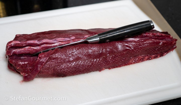 A freshly cut hare fillet resting on a white cutting board with a sharp knife beside it.