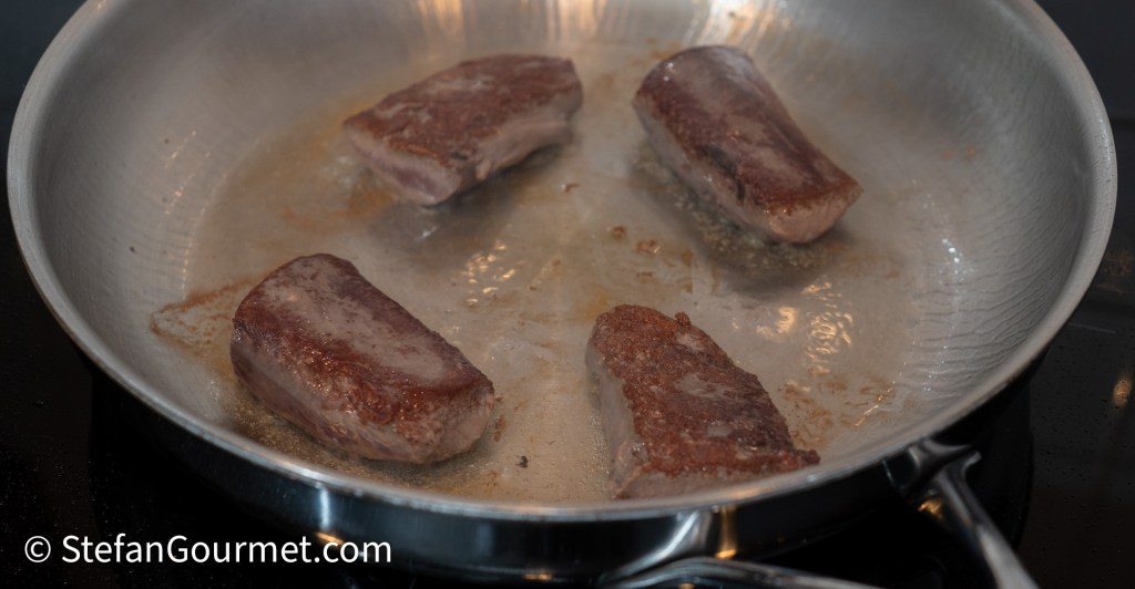 Searing hare fillets in a stainless steel frying pan, showcasing a golden-brown crust.