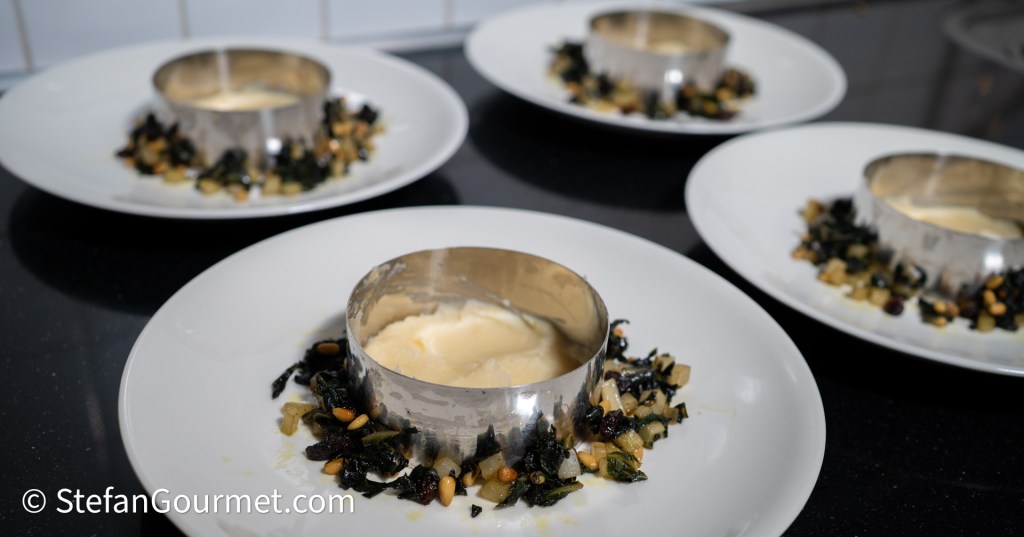 Plated dish featuring parsley root puree surrounded by sautéed chard, pine nuts, and raisins, served in metal rings.