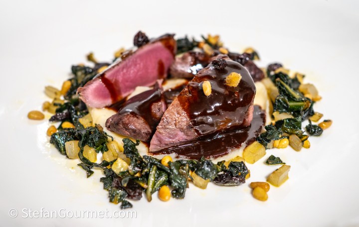 A beautifully plated dish featuring hare fillet with a rich chocolate jus, served alongside sautéed chard, pine nuts, and raisins on a bed of smooth parsley root puree.