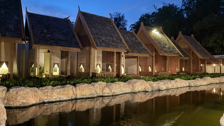 A serene view of individual dining cabins at Pak Tai restaurant in Koh Samui, Thailand, situated along a tranquil pond, with lush greenery and soft evening lighting.