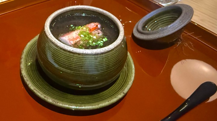 A bowl of chawanmushi, a savory egg custard dish, presented on a decorative tray. The chawanmushi contains crab surimi and is garnished with chopped green onions.