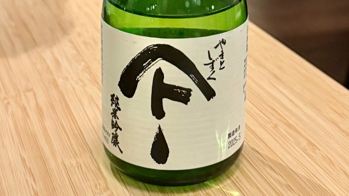 A bottle of sake with a minimalist label featuring Japanese characters, placed on a wooden surface.