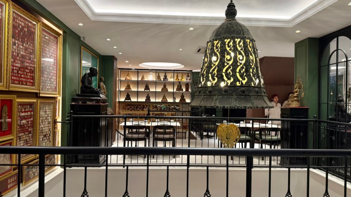 Interior view of a restaurant in Phuket, Thailand, showcasing ornate decorations, a large bell feature, shelves with statues, and dining tables.