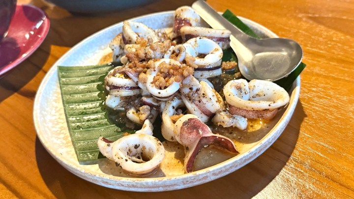 A dish of stir-fried squid garnished with crispy fried shallots, served on a banana leaf in a white plate.