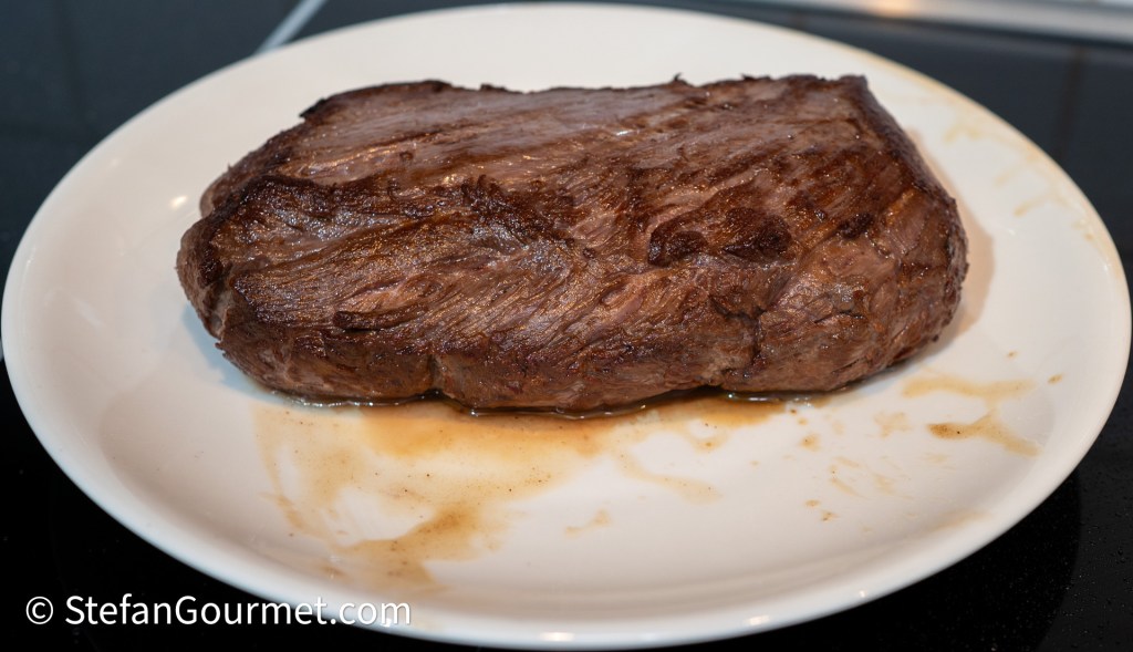 A perfectly cooked piece of beef, resting on a white plate with juices around it.