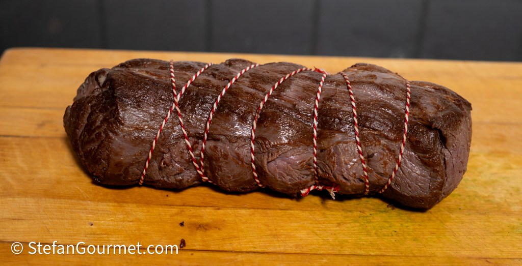 A tied roast of meat resting on a wooden cutting board.