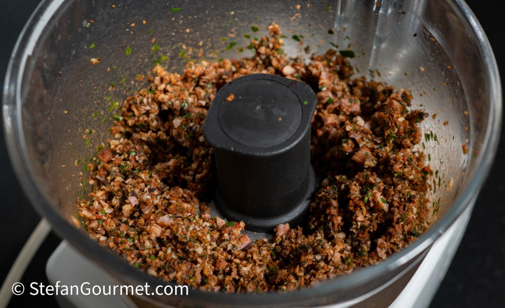 Chopped mixture of herbs, nuts, and spices in a food processor bowl.
