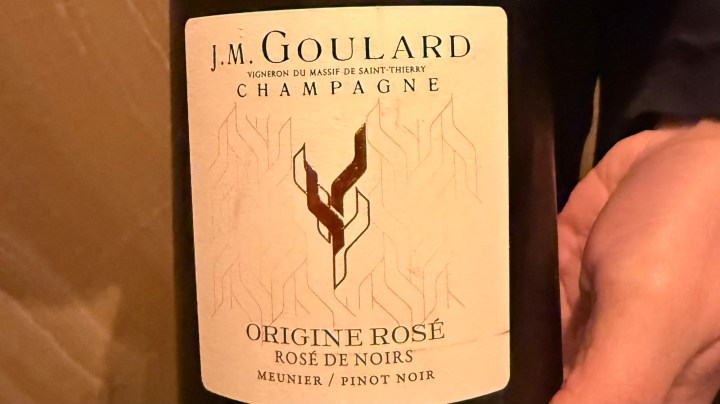 A close-up of a champagne bottle label featuring J.M. Goulard, highlighting 'Origine Rosé' and 'Rosé de Noirs' with the varietals Meunier and Pinot Noir.