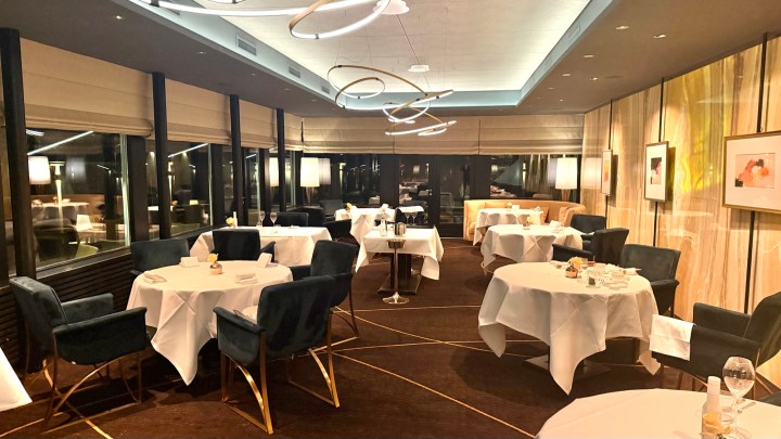 Elegant restaurant interior with dining tables set for guests, featuring modern lighting and large windows.