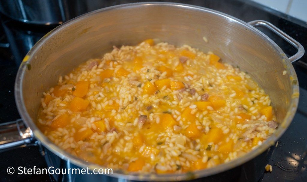A pot of creamy pumpkin risotto with pieces of squash and meat cooking on a stovetop.
