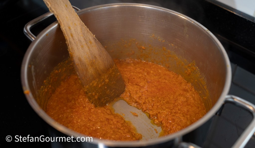 A pot with a thick, orange-brown sauce being stirred with a wooden spoon.