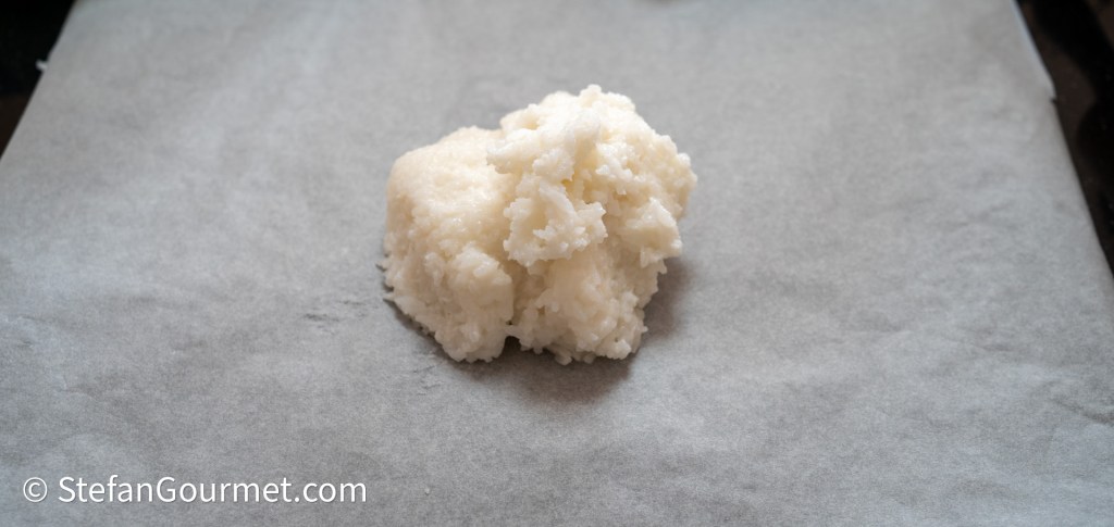 A lump of white dough or mixture on a sheet of parchment paper.