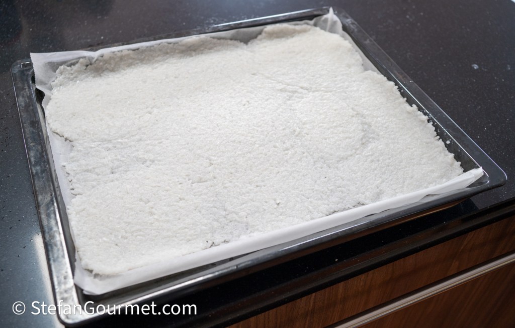 A baking tray lined with parchment paper containing a thick layer of white coconut flakes.