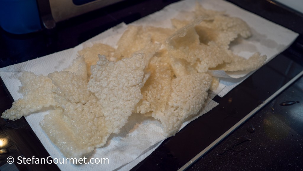 A close-up of crispy, translucent rice crackers arranged on a paper towel, placed on a dark countertop.