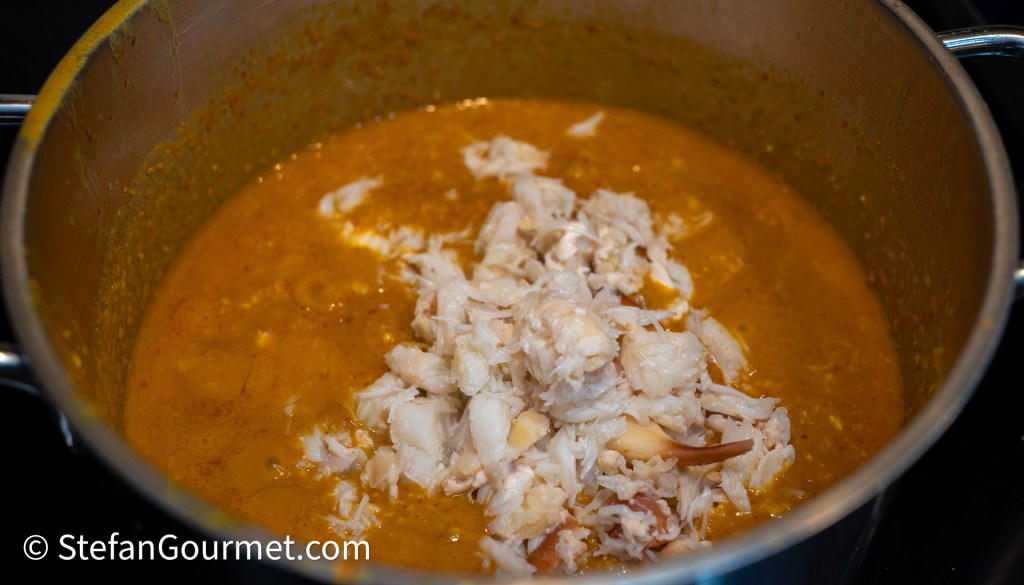 A pot filled with a golden brown sauce, featuring chunks of shredded crab meat being mixed in.