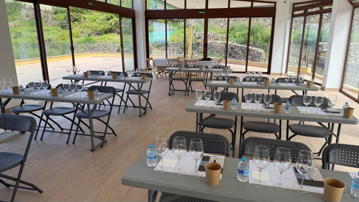 Interior view of a spacious event room with multiple tables set for a wine tasting, featuring glasses, water bottles, and notepads.