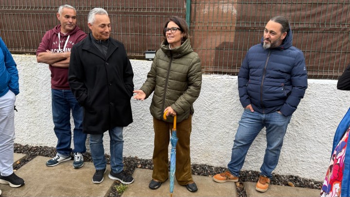A group of four adults engaged in conversation outdoors, with one woman speaking animatedly while holding an umbrella.