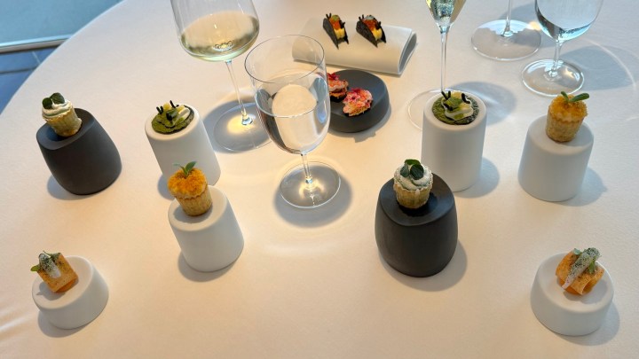 An elegantly arranged table featuring small gourmet appetizers on minimalist pedestals, complemented by glasses of sparkling wine and a central glass of water.