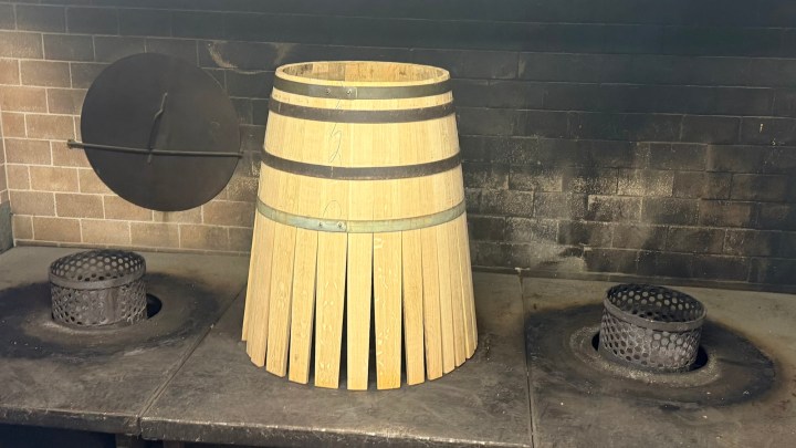 A wooden barrel placed upright on a blackened stove, with two circular metal containers nearby.