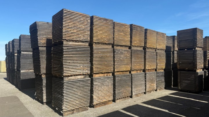 Stacked wooden pallets in a storage area under a clear blue sky.