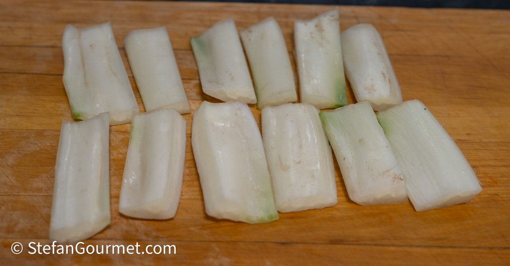 Sliced pieces of a white vegetable arranged on a wooden cutting board.