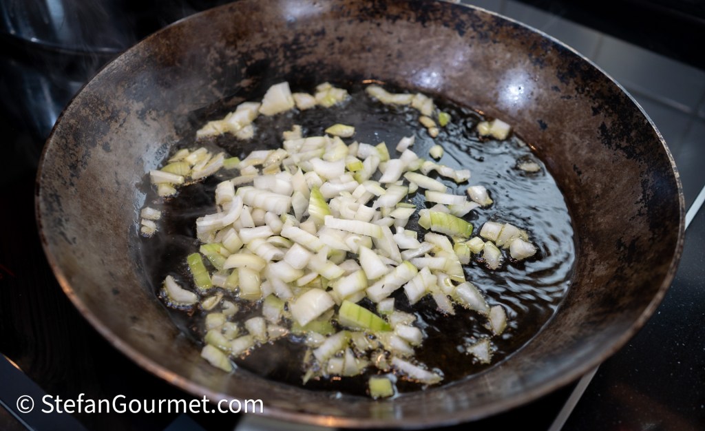 Chopped onions and leeks sautéing in a frying pan with hot oil.