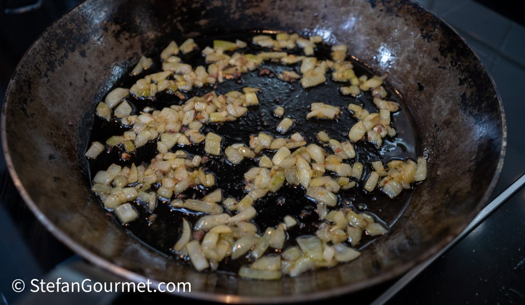 Sautéed diced onions cooking in a black frying pan with oil.