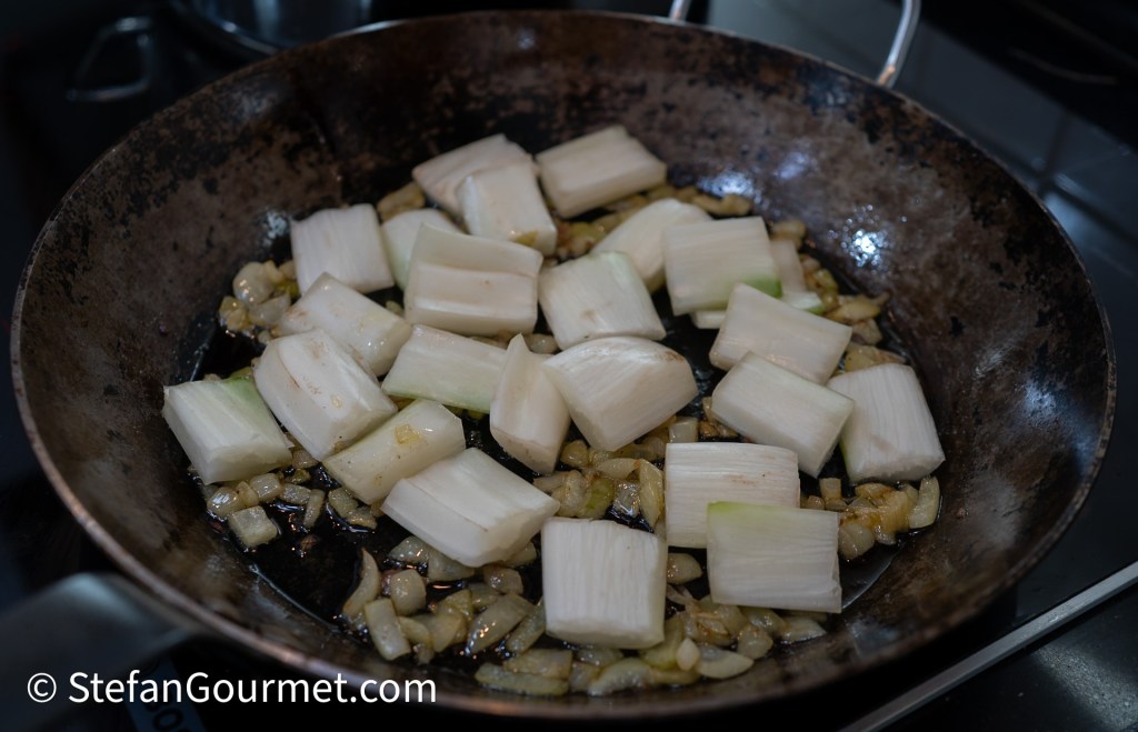 Chopped leeks sautéing with diced onions in a frying pan.