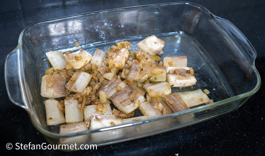A glass baking dish containing diced vegetables, including leeks and onions, sautéed until golden brown.