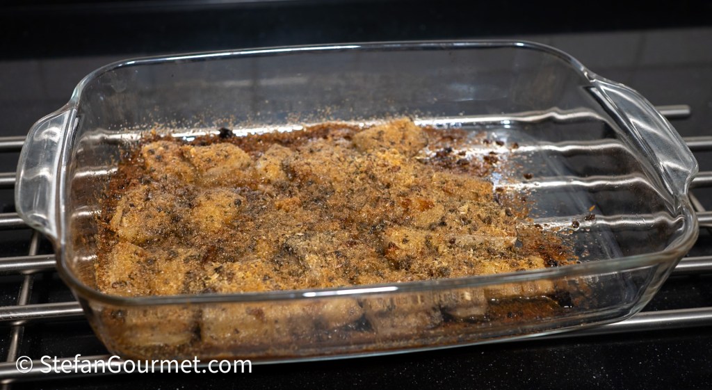 A glass baking dish containing baked food, with a crispy topping and some browned edges, placed on a cooling rack on a countertop.
