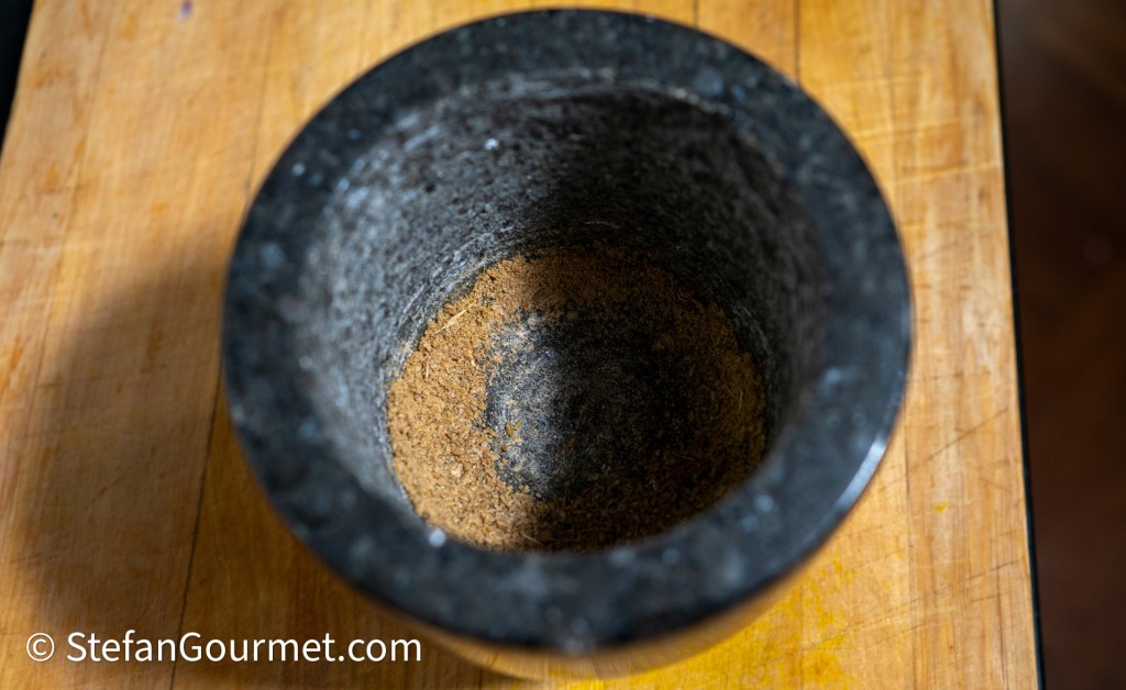 A close-up view of a granite mortar with finely ground spices inside, placed on a wooden surface.