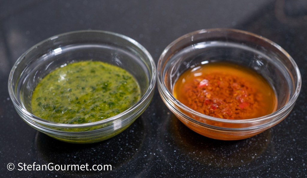 Two small glass bowls containing sauces, one green and herb-based, the other a reddish oil with spices.