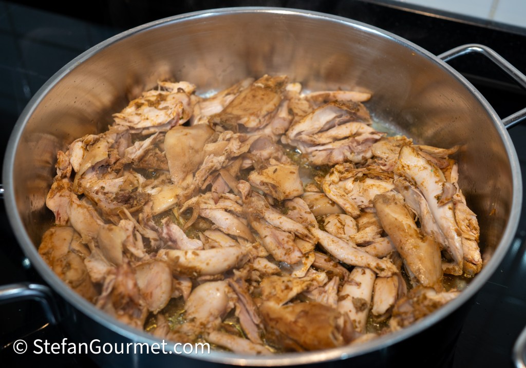 Close-up of shredded cooked chicken in a stainless steel pot, seasoned and simmering.