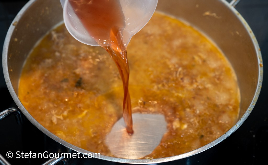 Pouring liquid into a pot of simmering broth on a stovetop.