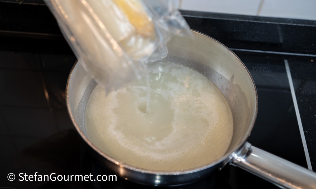A hand pouring a stick of butter from its packaging into a pot of melting butter on a stove.