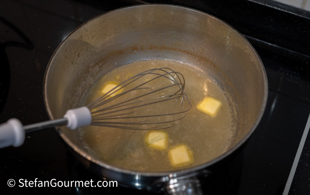 Melted butter cubes in a saucepan with a whisk, set against a stovetop.