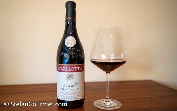 A bottle of Cavallotto Barolo wine alongside a filled wine glass on a wooden surface.