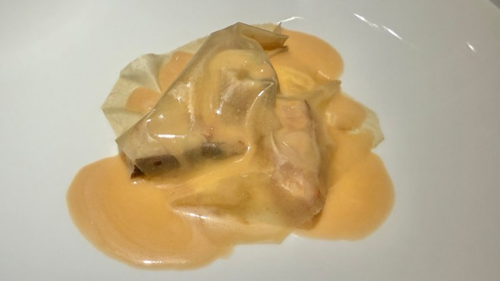 A gourmet dish featuring a delicate parcel of food covered in a creamy sauce, presented on a white plate.